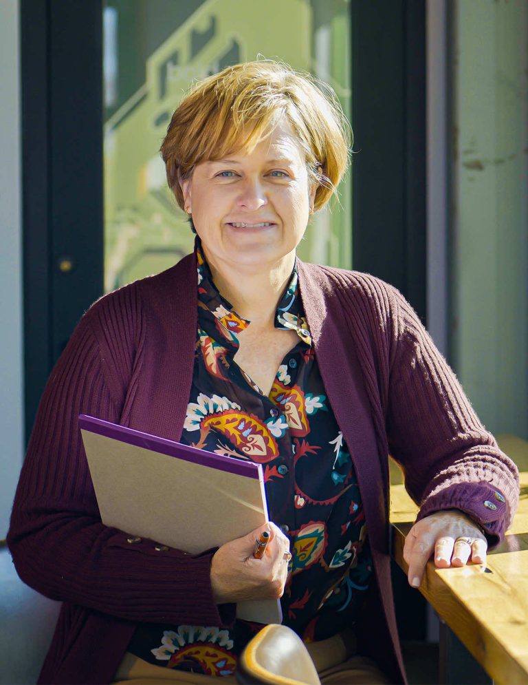 Image of Business Office Manager Karen Thacker in black floral blouse holding legal pad at Paradigm Digital Group offices