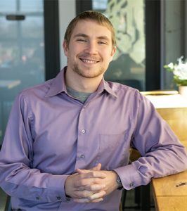 Image of Video Editor Samuel Jennings in purple button down sitting at Paradigm Digital Group office